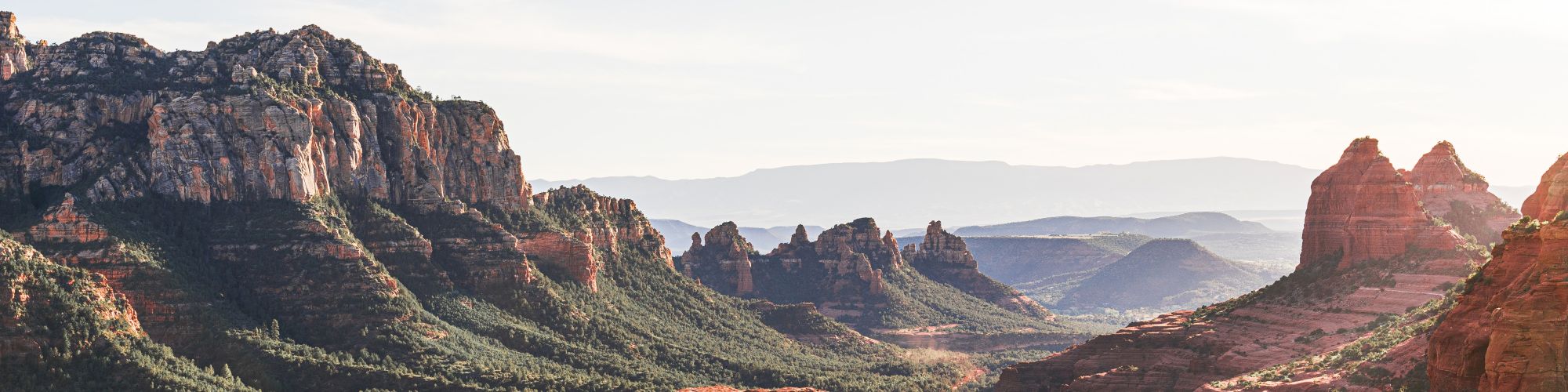 The image features a scenic landscape with red rock formations, a green valley, and mountains under a clear sky, likely taken during the daytime.