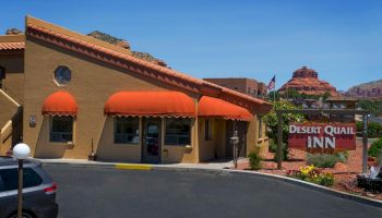 The image shows the Desert Quail Inn, a building with orange awnings, a parking lot, and scenic red rock formations in the background.